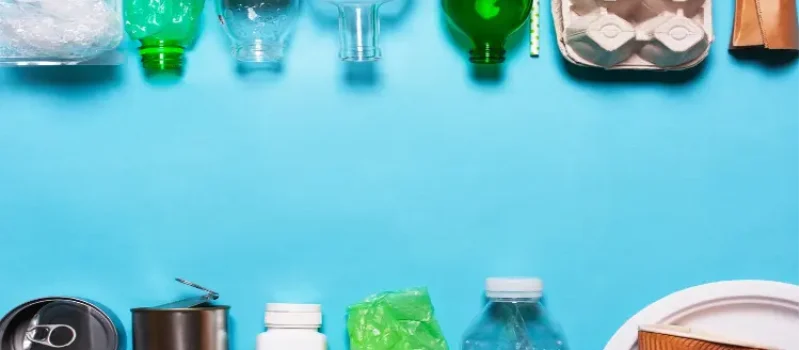 Række af forskellige genbrugelige plastflasker på en blå baggrund, herunder klare og grønne vandflasker og hvide mælkebeholdere, illustrerer genanvendelse af plastemballage.